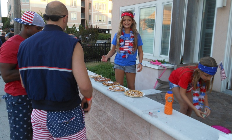 Isabella Georgelas, 11, smiles for the camera while her sister Athena makes change for Zach Rendin (sunglasses) and Ryan Crabbe who were buying the girl's fried dough. The sisters were selling the fried goodies to passersby so they good make a donation to the Wounded Warriors Project. BY CHRIS FLOOD